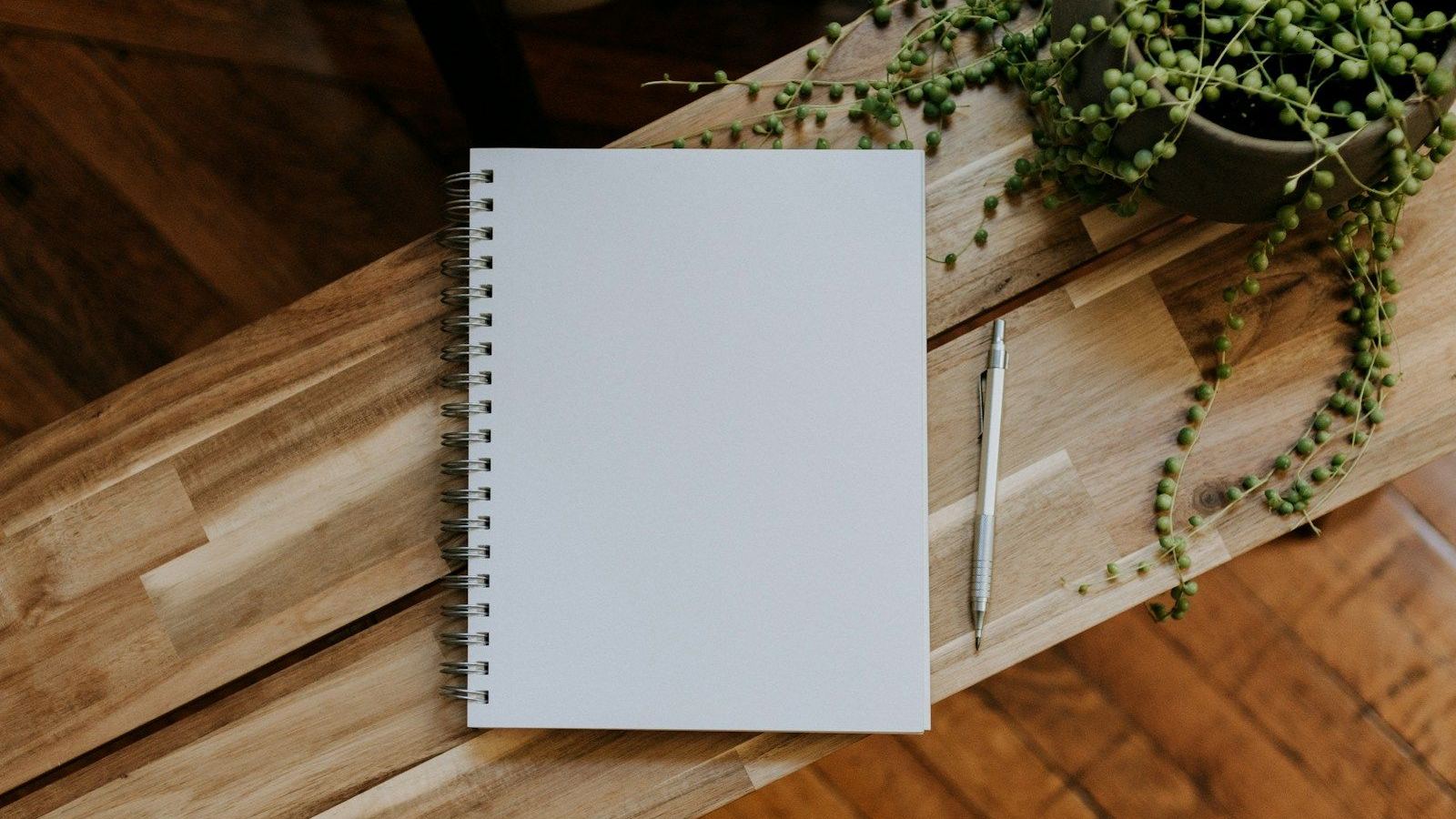 A blank notebook beside a potted plant
