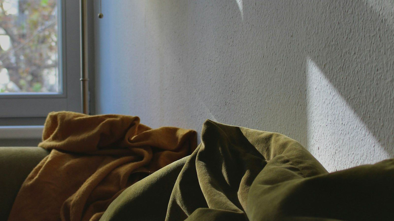 A blanket and cushions on a sofa by a window